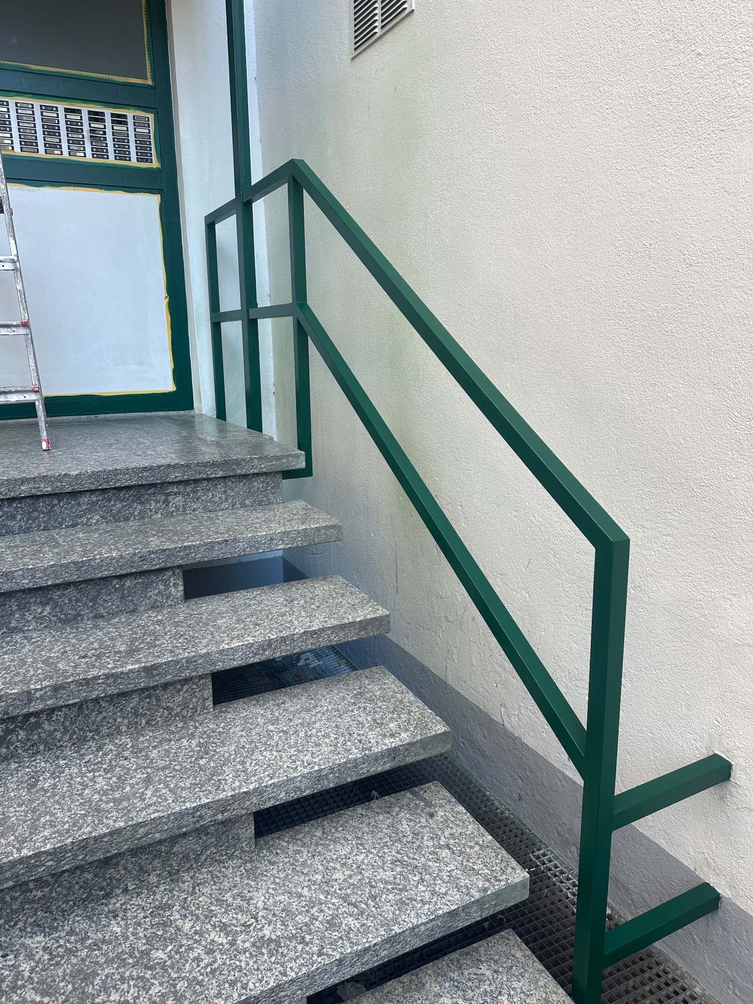 Frisch lackiertes grünes Geländer an Granitstufen