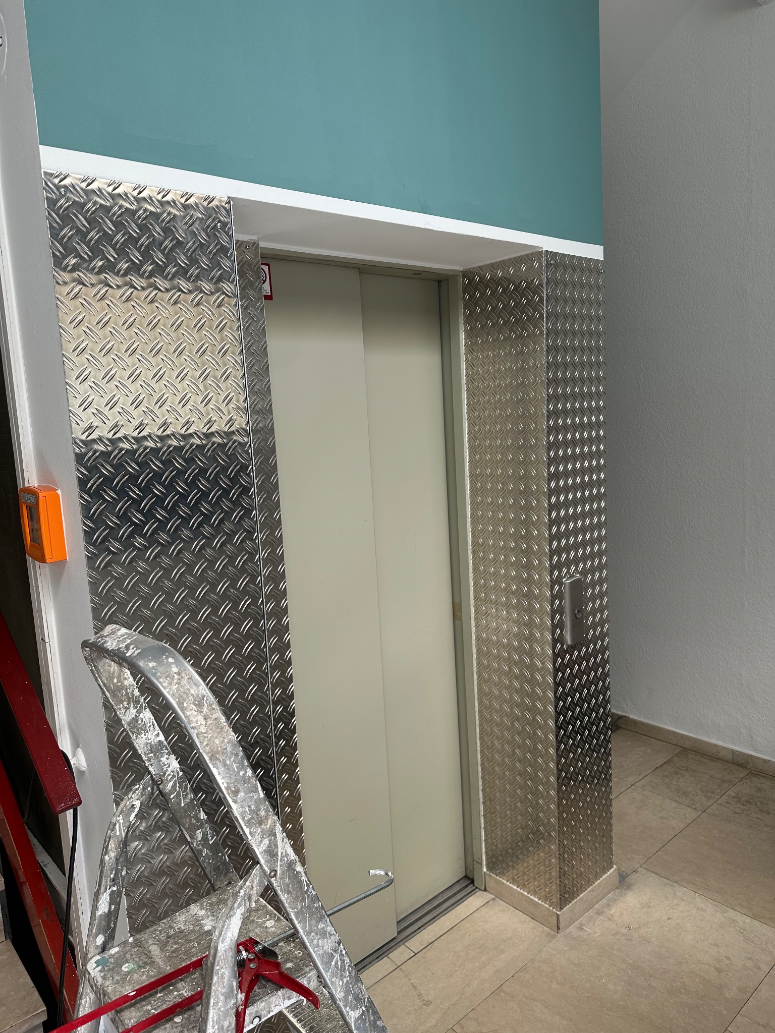 Renovierter Aufzugsbereich mit Trittblech-Verkleidung und türkisfarbener Wand